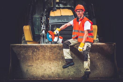 Bulldozer Works Concept. Young Caucasian Men Seating and Relaxing on Bulldozer Blade. Happy Construction Worker. Ground Works.