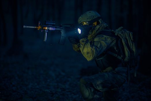 Military Night Operation. Soldier with Assault Rifle and Flashlights at Night.