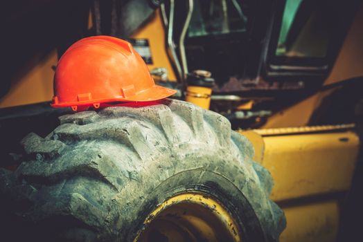 Work Safety Concept. Safety While Construction Working. Orange Safety Construction Helmet on  Large Heavy Duty Tractor Tire.