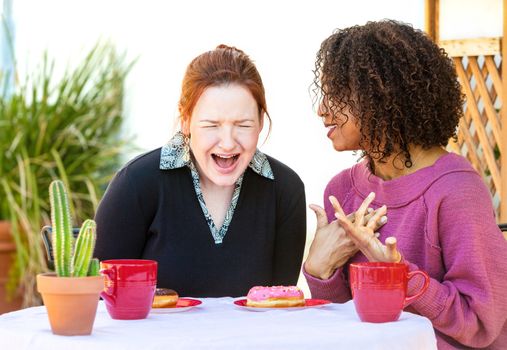 Two adult female friends talking about something funny while snacking