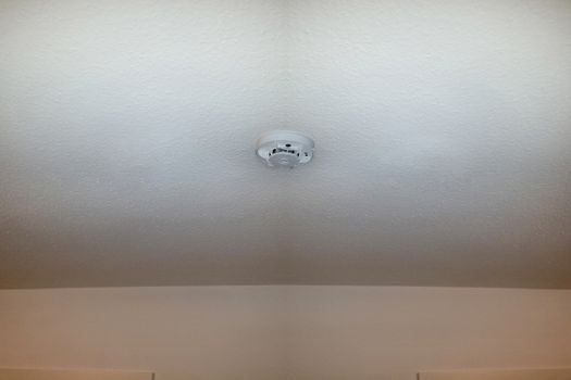 Smoke detector on the ceiling with red warning light sensor and smoke.