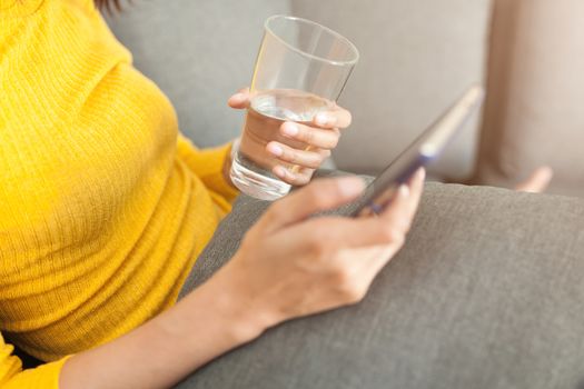 Beautiful woman holding a glass of water and using smartphone.