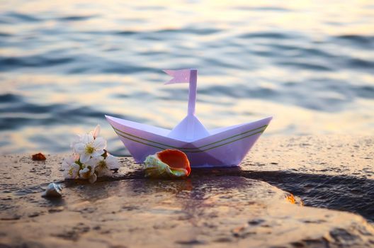 Paper boat, seashells and a sprig of cherry blossoms on a large stone on the seashore