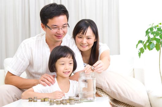 Asian mother and her kid putting coins together into the glass bottle