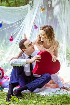 Smiling man and woman sitting on the ground and holding large decorative red heart in Lviv, Ukraine.