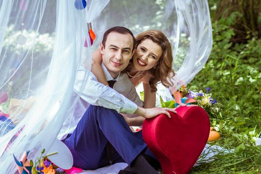 Smiling man and woman sitting on the ground and holding large decorative red heart in Lviv, Ukraine.