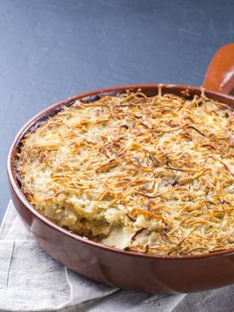 Close up view of appetizing potato casserole with fish, eggs and cream. Potato casserole in serving baking pan on dark concrete background