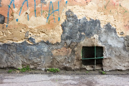 iron window on an old, chipped wall with graffiti on the level of the asphalt road