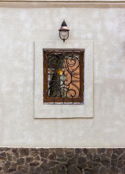 window with wrought protection and a lantern on the wall with a stone basement