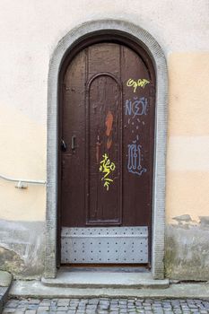 old wooden door with drawings, metal lock stitching, in the stone arch dilapidated walls of an old cobblestone street