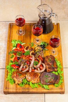 a huge number of all kinds of grilled meat and fried sausages with eggplant and tomato grl, olives and other herbs. Decanter and three glasses of wine on a wooden board.