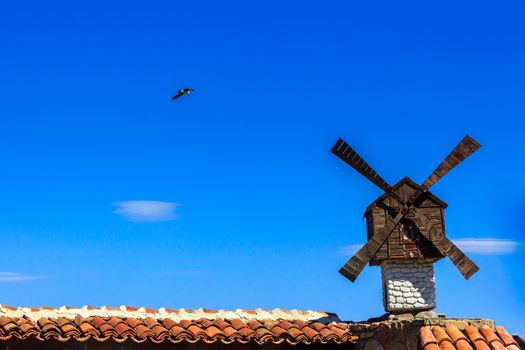 decorative windmill installed at the Architecture building on a background of the clear sky with a flying seagull