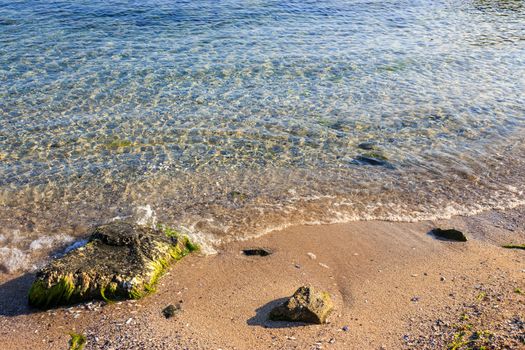 clean and clear sea waves wash sandy beach with few rocks