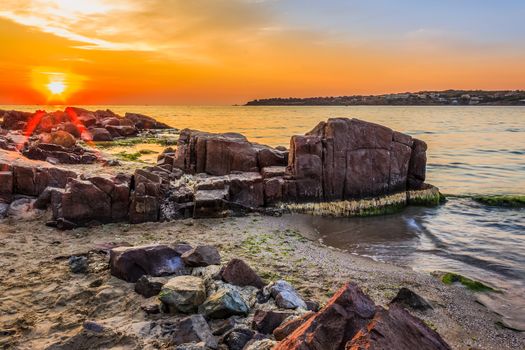 landscape red sun rise over the sea on the sandy beach with rocks and seaweed