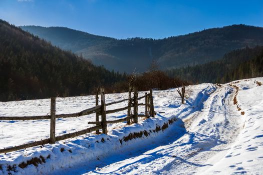 winter mountain landscape. winding road that leads into the pine forest covered with snow. wooden fence stands near the road.