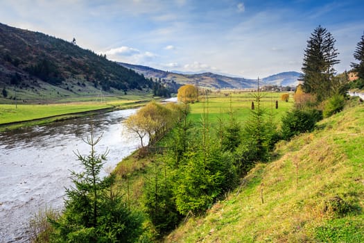 fields and trees along the river which flows at the foot of the mountains in autumn landscape