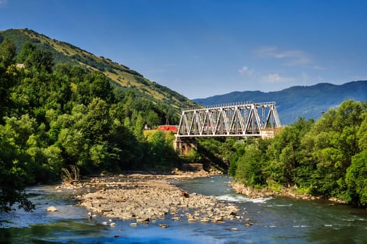 white metal bridge over the river in the mountains on serene summer day