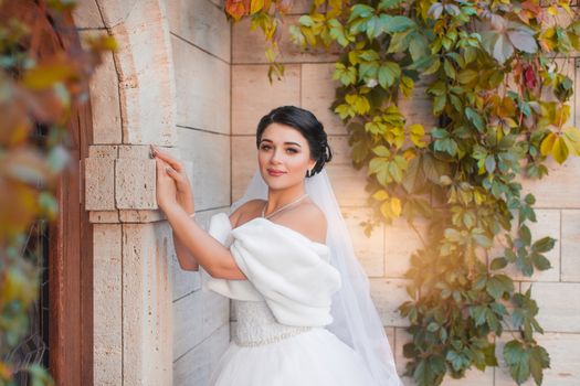 Stylish bride stands by the brick wall, posing on the photo