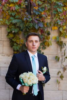 Happy bridegroom in a stylish suit against a brick wall background