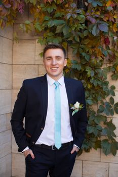 Happy bridegroom in a stylish suit against a brick wall background