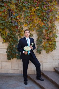 Happy bridegroom in a stylish suit against a brick wall background