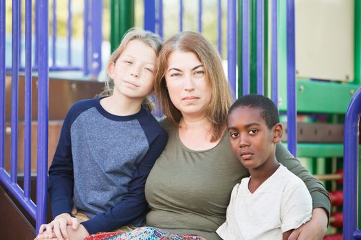 Adult woman sitting with handsome male children on playground equipment