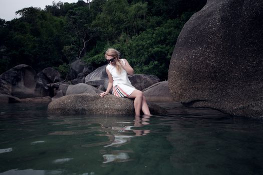 portrait of girl sitting on rock and looking on water