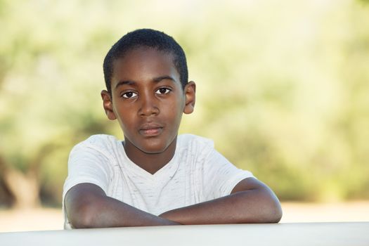 Serious African child seated at table with folded arms