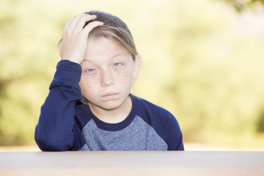 Sad or sick little boy with freckles and hand on head