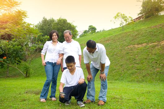 Asian three generation family inspecting leaf with magnifying glass in the park. Healthy lifestyle concept.