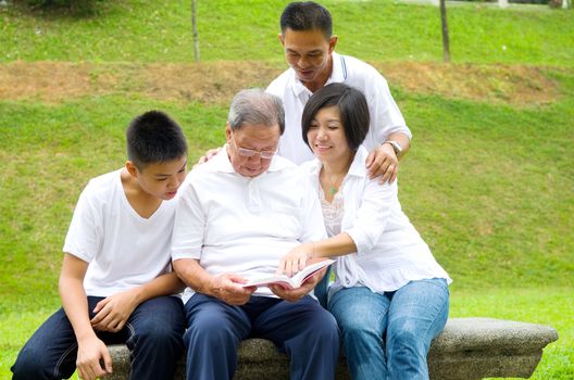 Asian three generation family reading book at outdoor park