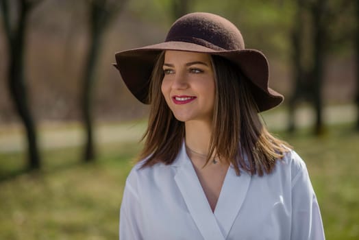 Portrait of a smiling young woman who's looking away and wearing a hat in a park during spring. Medium shot. Shallow depth of field.