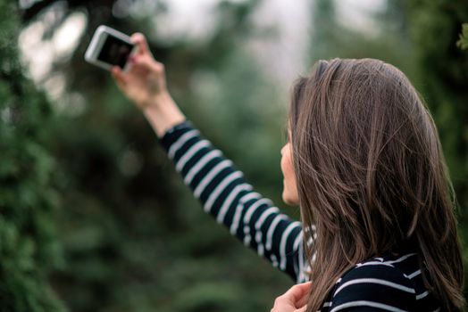 Young girl in striped sweater is taking picture of herself in the park. Shallow depth of field.