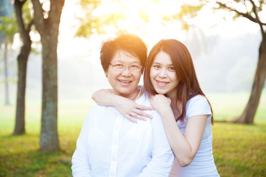 Portrait of Asian elderly mother and daughter, senior adult woman and grown child. Outdoors family at nature park with beautiful sun flare.