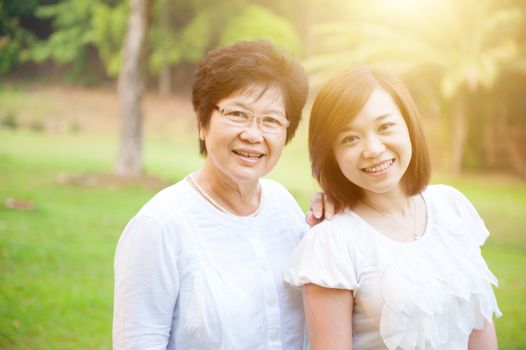 Portrait of attractive Asian elderly mother and daughter, senior adult woman and grown child. Outdoors family at nature park with beautiful sun flare.