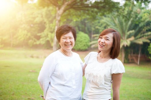 Portrait of Asian elderly mother and daughter talking, senior adult woman and grown child. Outdoors family at nature park with beautiful sun flare.