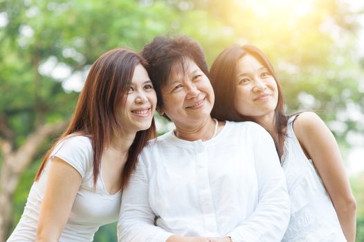 Portrait of happy Asian elderly mother and her daughters, senior adult woman and grown child. Outdoors family at nature park with beautiful sun flare.
