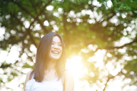 Portrait of happy Asian woman smiling at outdoor park, morning sun flare background.