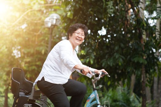 Active elderly Asian woman cycling, senior adult activity, riding bike outdoor in morning.