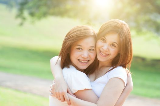 Young Asian sisters having fun at outdoor park, friendship concept, sun flare background.