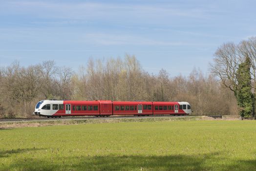 Red white colored train on a light rail track in the Achterhoek near Winterswijk in the Netherlands
