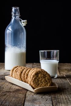 Milk and chocolate cookies on an old wooden table, black background