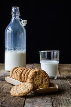 Milk and chocolate cookies on an old wooden table, black background