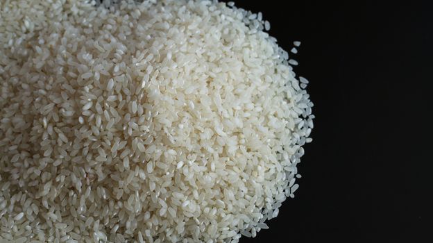 Pile of rice spill on black background. Agriculture food raw seed. Closeup macro photo