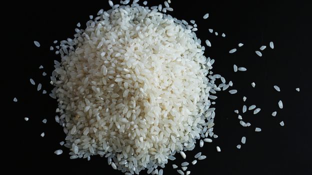 Round pile heap of rice or wholegrain spill on black background. Agriculture food raw seed. Closeup macro photo