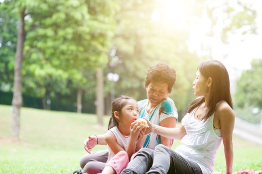 Candid portrait of multi generation Asian family at nature park. Grandmother, mother and daughter outdoor fun. Morning sun flare background.