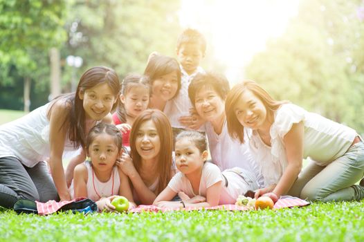Happy Asian multi generations family portrait, grandparent, parents and children, outdoor nature park in morning with sun flare.