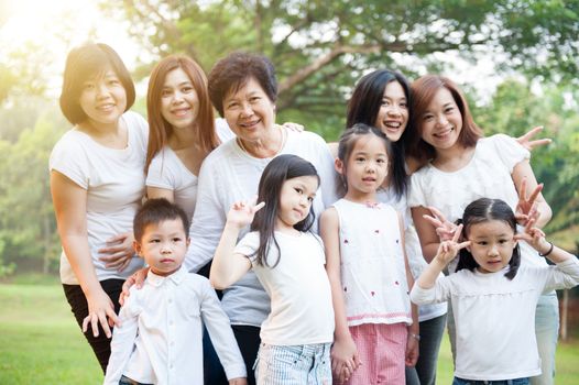 Group of cheerful Asian multi generations family portrait, grandparent, parent and children, outdoor nature park in morning with sun flare.