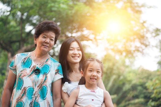 Portrait of happy multi generations Asian family at nature park. Grandmother, mother and daughter outdoor fun. Morning sun flare background.