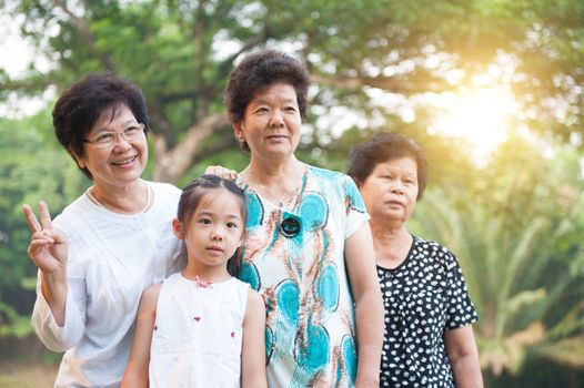 Portrait of beautiful multi generations Asian family at nature park. Grandmother and grandchild outdoor fun. Morning sun flare background.